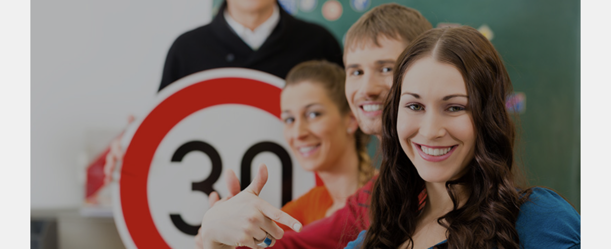 Lächelnde Gruppe junger Erwachsener mit Tempo-30-Schild – Erste Hilfe für Fahrschüler